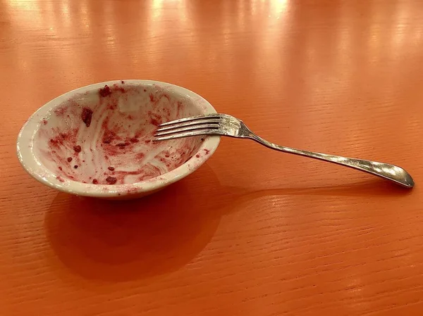 Töm tallrik med spår av dessert. Vit använde rätter på ett brunt bord. Tallrik med gaffel efter äten sallad. — Stockfoto