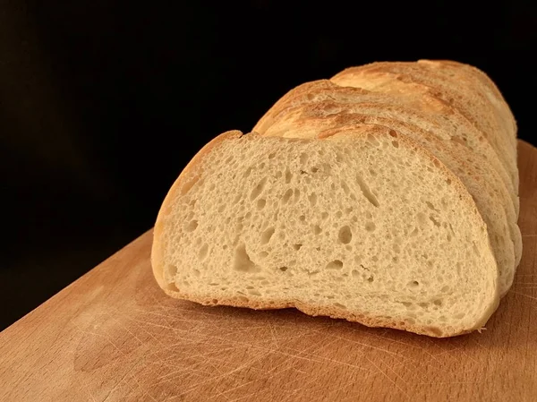 Dilimlenmiş buğday ekmeği masanın üstünde duruyor, siyah arkaplan. Mutfak tahtasının üzerinde beyaz ekmek var. Ev yapımı yemek pişirme.. — Stok fotoğraf