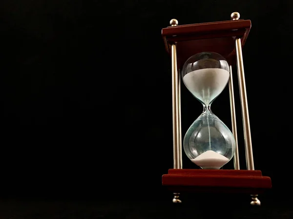 Пісочний годинник на підставці, чорний фон. Скляний пісочний годинник у гільзі. Вимірювач часу скла. Концепція: час закінчується, управління часом — стокове фото