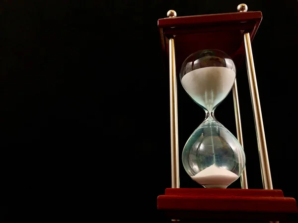 Hourglass on a stand, black background. Glass hourglass in the case. Glass time meter. Concept: time is running out, time management — Stok fotoğraf