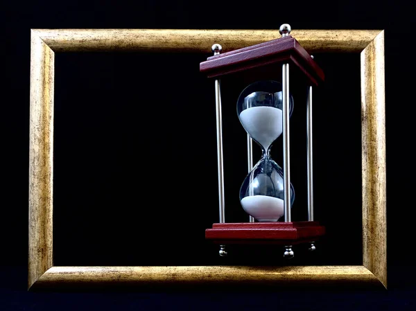 Hourglass in a wooden frame, on a black background. Glass hourglass in a frame for a picture. Glass time meter. Concept: time is running out, time management
