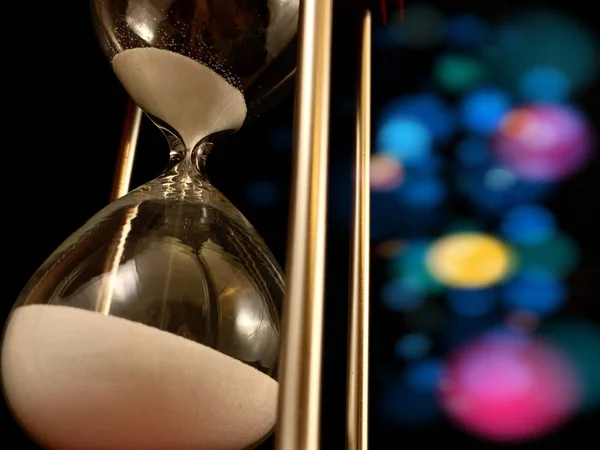 Hourglass on a stand, black background. Glass hourglass in the case. Glass time meter. Concept: time is running out, time management — Stok fotoğraf