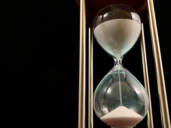 Hourglass on a stand, black background. Glass hourglass in the case. Glass time meter. Concept: time is running out, time management — Stok fotoğraf
