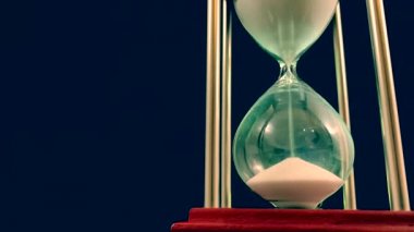 Hourglass on a stand, black background. Glass hourglass in the case. Glass time meter. Concept: time is running out, time management, time value