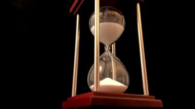 Hourglass on a stand, black background. Glass hourglass in the case. Glass time meter. Concept: time is running out, time management, time value