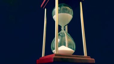 Hourglass on a stand, black background. Glass hourglass in the case. Glass time meter. Concept: time is running out, time management, time value