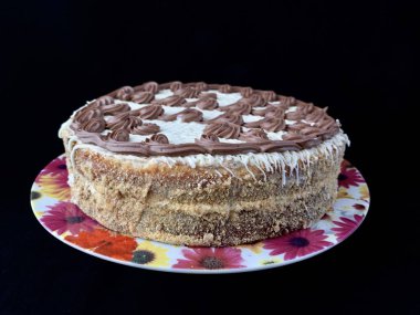 Krem desenli yuvarlak pasta, siyah arka planda. Bir ergen için güzel bir doğum günü hediyesi. Tüm aile için şenlikli bir tatlı. Tabakta kremayla pişirme.