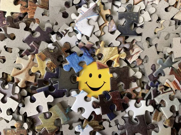 Colorized smile on the background of paper puzzles. Image of a happy face on cardboard. Puzzle in detail in a mosaic set. Concept: joy, happiness, positive.