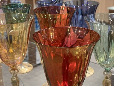 Mağazadaki bir rafta renkli şarap bardakları. Şeffaf camdan yapılmış içecekler için cam eşyalar. Tatil için kristal bardaklar.