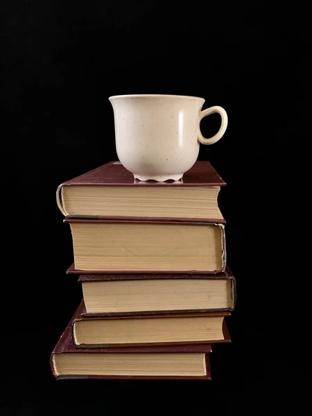 Libros cerrados y una taza de café sobre un fondo negro. Una taza de té y un libro de tapa dura . — Foto de Stock