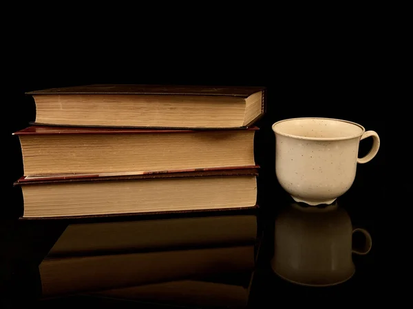 Zamknięte książki i filiżanka kawy na czarnym tle. Filiżankę herbaty i twardą książkę.. — Zdjęcie stockowe