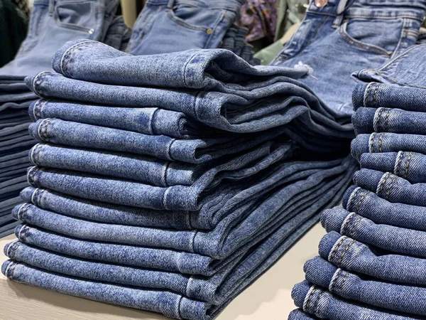 Piles of modern jeans of different sizes. A selection of jeans in a clothing store. Shelves with clothes in the department of cotton products.