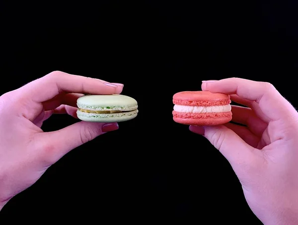 Bunte leckere Macarons in den Händen auf schwarzem Hintergrund. köstliche französische Mandeln auf einem Mädchen. Dessert, hausgemachte Kuchen. — Stockfoto