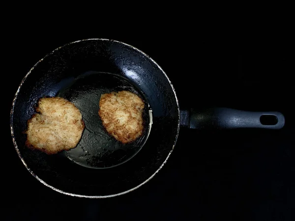 Картофельные блинчики в процессе приготовления. Жареные блинчики на старой сковороде, на черном фоне. Готовые пироги на сковороде в масле . — стоковое фото