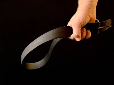 Bir adamın elinde cezalandırmak için siyah bir arka planda deri bir kemer. Adamın biri yumruğunda kemer tutuyor. Baba, çocuğu kemerle cezalandıracak. Kavram: Cezalandırma, Aile İçi Şiddet