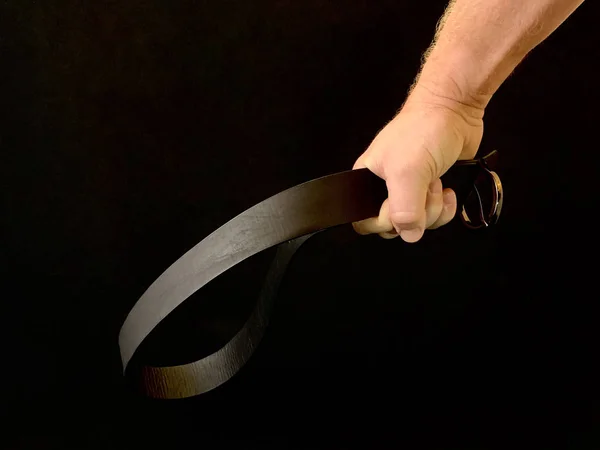 Bir adamın elinde cezalandırmak için siyah bir arka planda deri bir kemer. Adamın biri yumruğunda kemer tutuyor. Baba, çocuğu kemerle cezalandıracak. Kavram: Cezalandırma, Aile İçi Şiddet