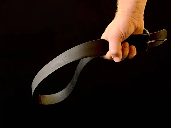 Bir adamın elinde cezalandırmak için siyah bir arka planda deri bir kemer. Adamın biri yumruğunda kemer tutuyor. Baba, çocuğu kemerle cezalandıracak. Kavram: Cezalandırma, Aile İçi Şiddet