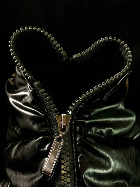 Background texture: zipper in a jacket in the shape of a heart. Opened lock on knitted fabric, on a black background.