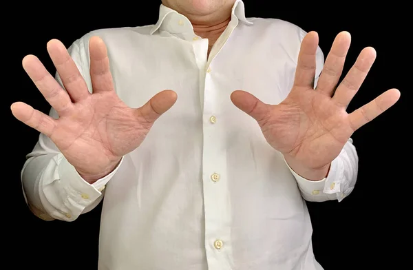 Um homem tem duas mãos à sua frente. Um homem de camisa branca mostra um gesto de mão, sobre um fundo preto. Conceito: medo, rejeição . — Fotografia de Stock