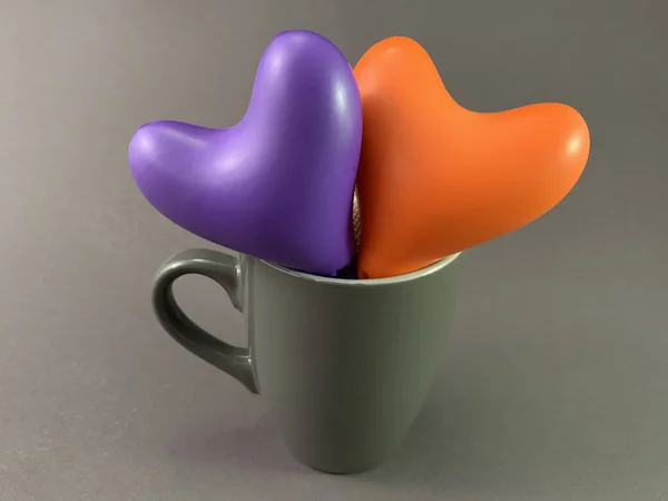 Två flerfärgade hjärtan i en kopp. Mugg med ett hjärta inuti, på en svart bakgrund. Koncept: kärlek, te för två, Alla hjärtans dag. — Stockfoto