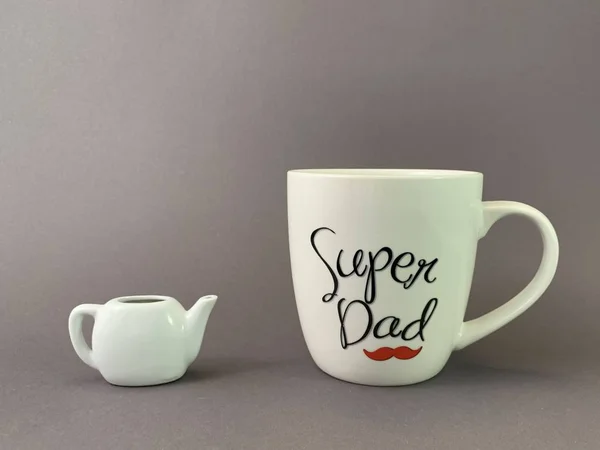 En stor kopp och en liten vattenkokare. En enorm mugg med inskriptionen. Koncept: super pappa. — Stockfoto