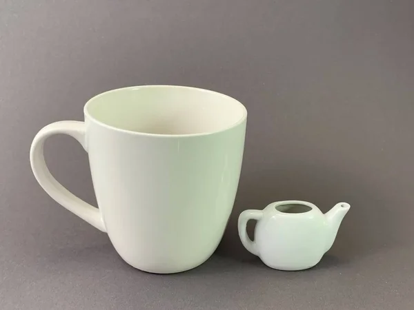 Velký šálek a malou konvici. Obrovský bílý hrnek na šedém pozadí. Koncept: čajové náčiní, čas na čaj. — Stock fotografie
