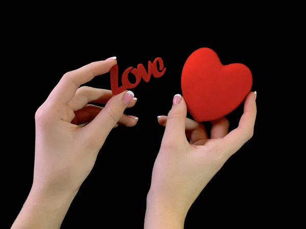 A inscrição "Amor" e um coração vermelho nas mãos de uma menina em um fundo preto. Uma mulher está segurando um sinal de coração com os dedos. Conceito: Dia dos Namorados, casamento e outros feriados . — Fotografia de Stock