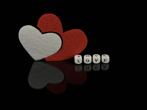 La inscripción "Amor" y un corazón rojo sobre un fondo negro. Reflejo de dos corazones de una superficie brillante. El concepto de San Valentín, bodas y otros días festivos . — Foto de Stock
