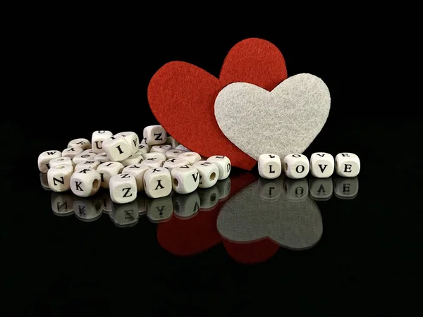 De inscriptie "Love" en een rood hart op een zwarte achtergrond. Reflectie van twee harten van een glanzend oppervlak. Het concept van Valentijnsdag, bruiloften en andere feestdagen. — Stockfoto