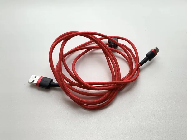 Red cord for charging a smartphone, on a white background. Accessory for phone, USB cable.