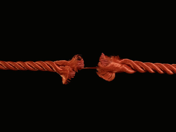 The torn rope is about to break, a black background. The rope is held on one thread. Concept: life in the balance.