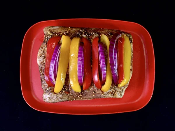 Siyah arka planda, sebzeli büyük bir parça kızarmış et. Biber ve baharatlı biftek pirzolası. Fırında pişirmek için domuz eti ve dana eti..