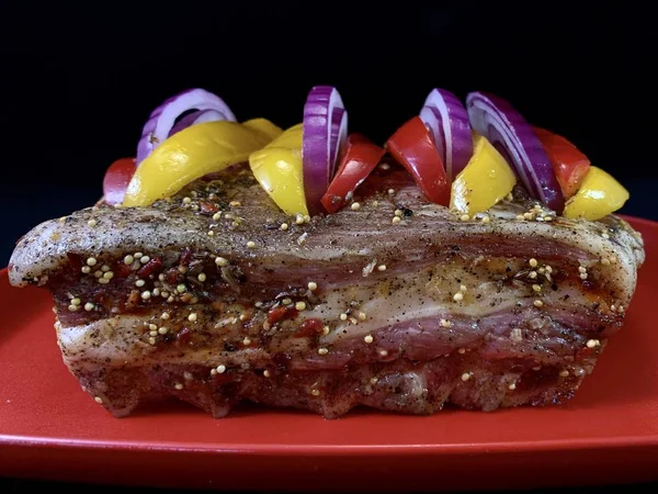 Un trozo grande de carne frita con verduras, sobre un fondo negro. Costillas de filete con pimiento dulce y especias. Cerdo y ternera para hornear en el horno . —  Fotos de Stock