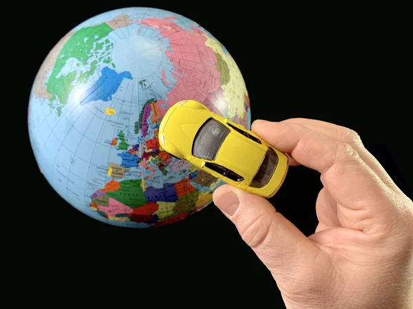 Zabawkowy samochód w ręku na tle globu. Mężczyzna z modelem samochodu, na czarnym tle. Mężczyzna wskazuje dłoń na kulę ziemską. Koncepcja: podróże, turystyka — Zdjęcie stockowe