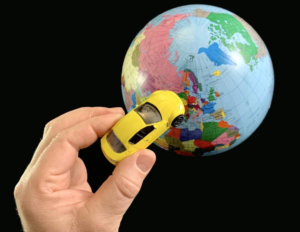 Speelgoedauto in de hand op een achtergrond van de aardbol. Man met een auto model, op een zwarte achtergrond. Een man wijst zijn hand naar de wereld. Concept: reizen, toerisme — Stockfoto