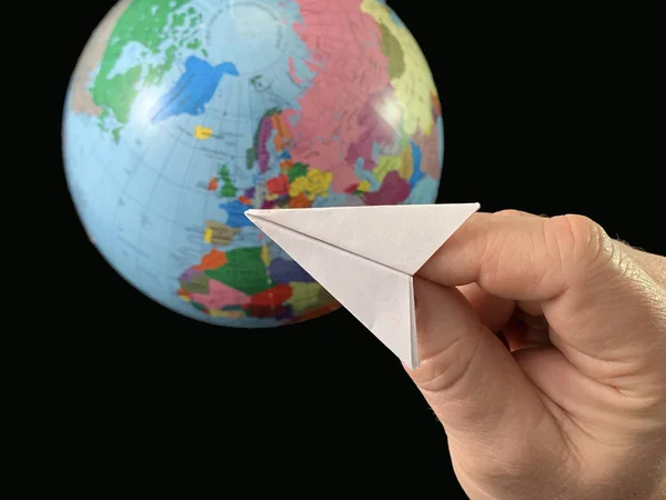 Papierflieger in der Hand auf einem Globus-Hintergrund, schwarzer Hintergrund. Flug des Flugzeugs um die Welt. Ein Mann zeigt mit der Hand auf die Erdkugel. Konzept: Reisen, Tourismus, — Stockfoto