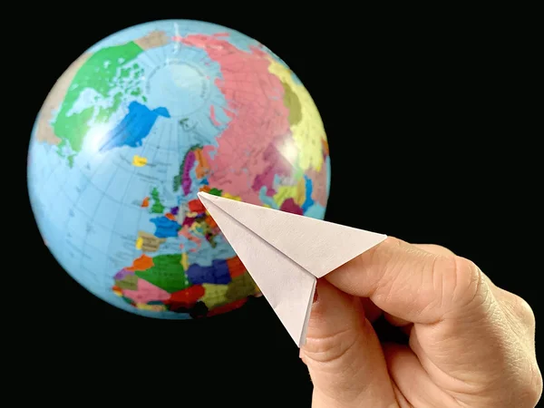 Avión de papel en la mano sobre un fondo del globo, fondo negro. Vuelo del avión en todo el mundo. Un hombre señala su mano al mundo. Concepto: viajes, turismo, —  Fotos de Stock