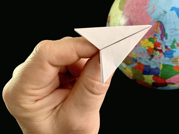 Papier vliegtuig in de hand op een globe achtergrond, zwarte achtergrond. Vlucht van het vliegtuig over de hele wereld. Een man wijst zijn hand naar de wereld. Concept: reizen, toerisme, — Stockfoto