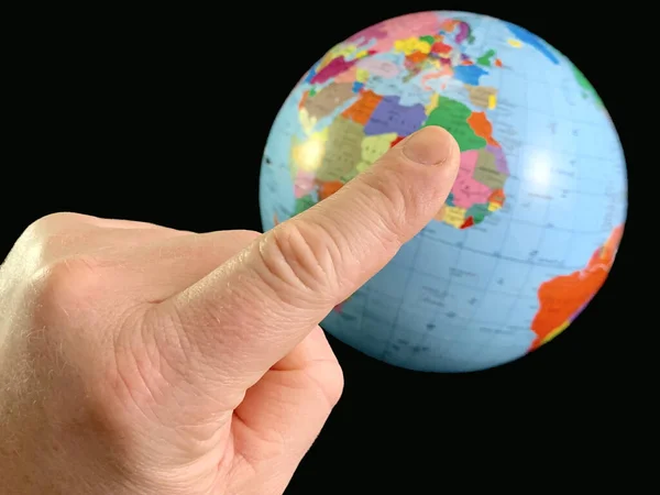 Index vinger wijst naar een wereldbol, op een zwarte achtergrond. Een vinger aanraken aan de aardbol. Een man houdt zijn hand in de richting van de wereldkaart. Concept: reizen, toerisme — Stockfoto