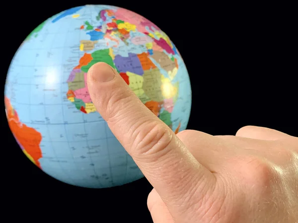 Index vinger wijst naar een wereldbol, op een zwarte achtergrond. Een vinger aanraken aan de aardbol. Een man houdt zijn hand in de richting van de wereldkaart. Concept: reizen, toerisme — Stockfoto