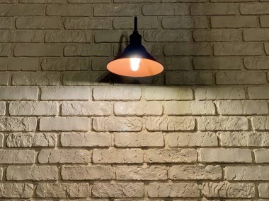 Beyaz tuğla bir duvarın arkasında büyük siyah bir lamba. Bir ampul siyah dikişli beyaz tuğla bir duvarı aydınlatır. Beyaz tuğla bir duvarın arka planında büyük siyah bir lamba. Ampul beyaz bir tuğla duvarı aydınlatıyor..