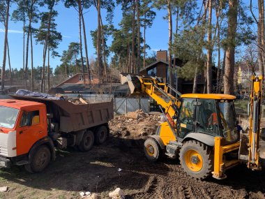 Yıkılmış tuğla evin yanında ağır ekipman var. Evin harabelerinin arka planında inşaat makineleri var. Kazıcılı eski bir evin yıkımı. Binanın ve kamyonun yıkılmış duvarları..