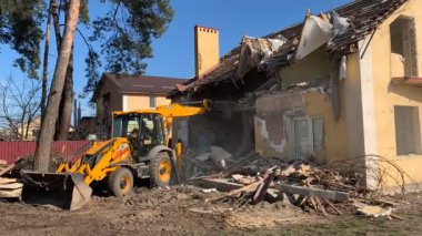 Yıkılmış tuğla evin yanında ağır ekipman var. Evin harabelerinin arka planında inşaat makineleri var. Kazıcılı eski bir evin yıkımı. Irpin, Kiev bölgesi, 13 Mart.