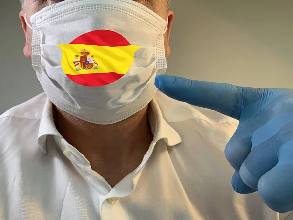 Man in medical mask with the flag of Spain. The male face is covered with a protective medical mask in a glove. Concept: coronavirus epidemic, spread of pneumonia, pandemic, Covid-19