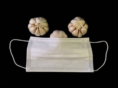 Siyah arka planda sarımsak ve tıbbi maske. Doğal vitaminler, karanlık bir masada antibiyotikler. Kavram: evde viral enfeksiyon ve korovirüsün önlenmesi.
