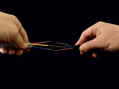 Erkek elinde bakır kablolar açılır. Siyah arka planda elektro kablolar var. Elektrikçi kabloları bağlıyor