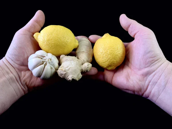 Garlic, ginger and lemon in the hands of a man. Natural vitamins in the palms of man, on a black background. Concept: Prevention of viral infections at home.