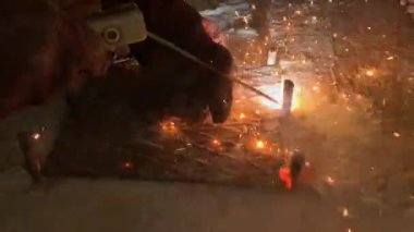 Kaynakçının işi sırasında kaynak makinesinden çıkan kıvılcımlar. Usta, metal bir çubuğu aletle lehimliyor. İşçi inşaatçısı güçlendirilmiş çeliği kesti.