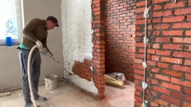 Sanatçı alçıyı tuğla duvara yapıştırıyor. İnşaatçı duvar kaplamalarıyla meşgul. Boyacı, alçı sprey tabancayla çalışıyor. Irpin, Kiev bölgesi, 20 Nisan 2020