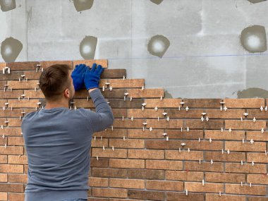 Masters evin ön cephesini döşedi. İnşaatçılar tuğla bir malikanenin duvarlarını süsler. Binayı modern malzemelerle dekore ediyor. Irpin, Kiev bölgesi, 9 Mayıs 2020